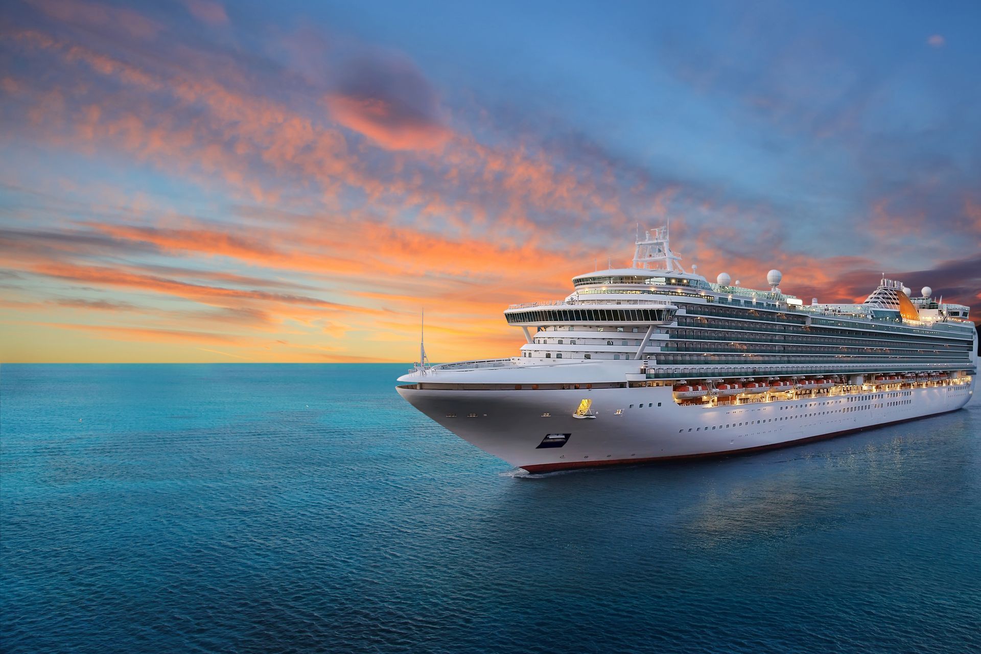 A cruise ship is sailing in the ocean at sunset.