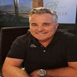 A man is sitting at a table with his arms crossed and smiling.
