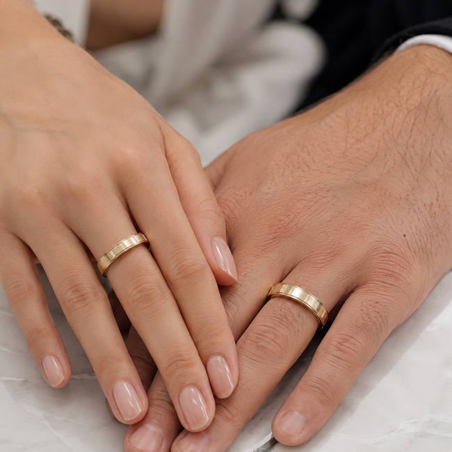 Dos manos con anillos de oro a juego descansando juntas sobre un fondo de tela blanca.