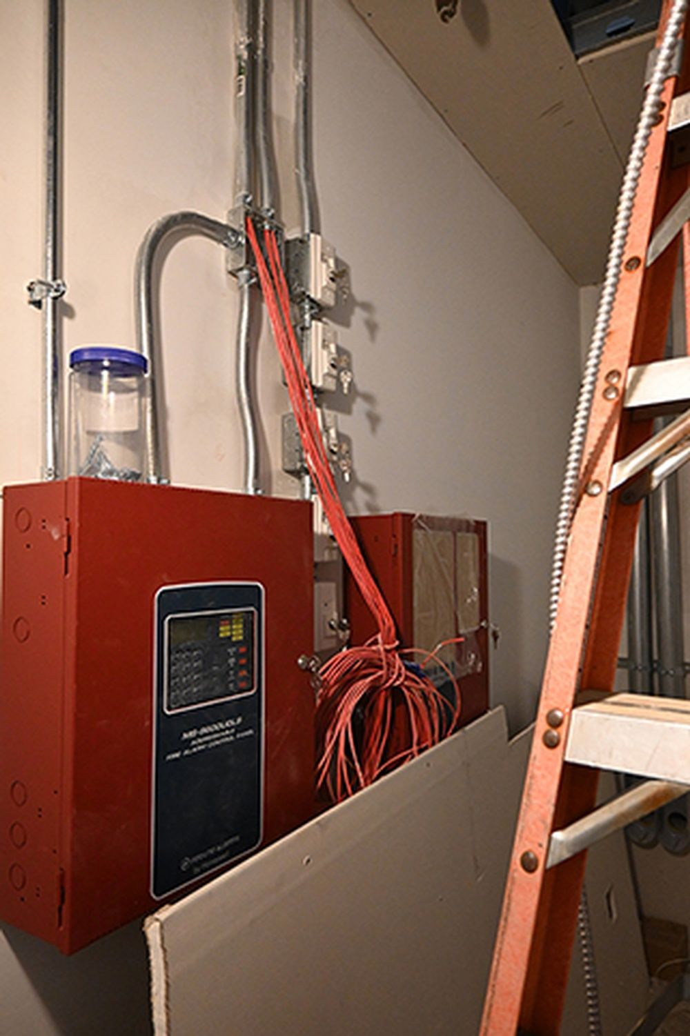 A ladder is leaning against a wall next to a fire alarm box.