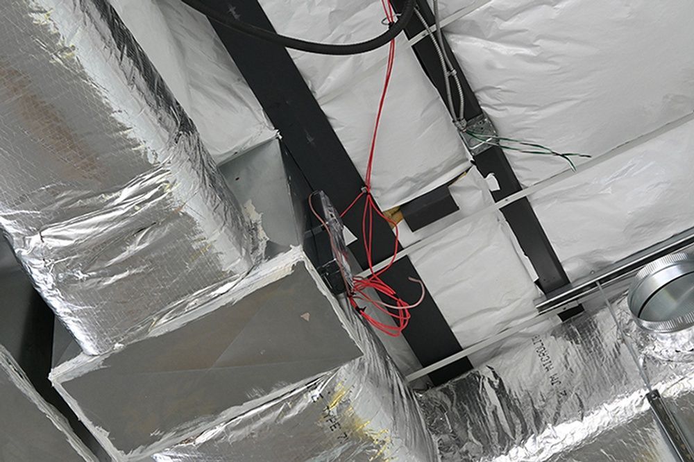 A close up of a ceiling with ducts and wires.
