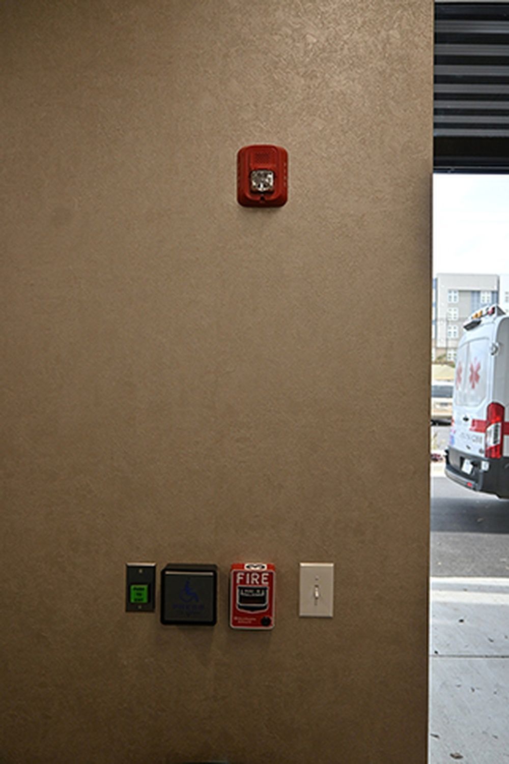 A fire alarm is hanging on a wall next to a van.