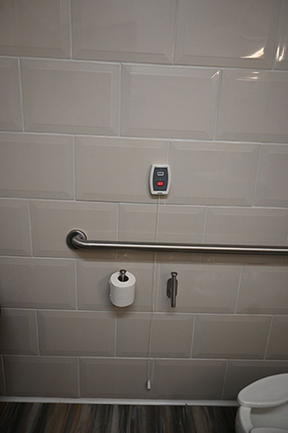 A bathroom with a toilet , a roll of toilet paper , and a hand rail.