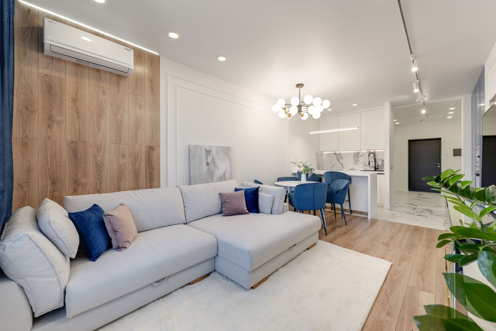 Bright modern living room with gray sectional, blue chairs, wood accent wall, and open kitchen area