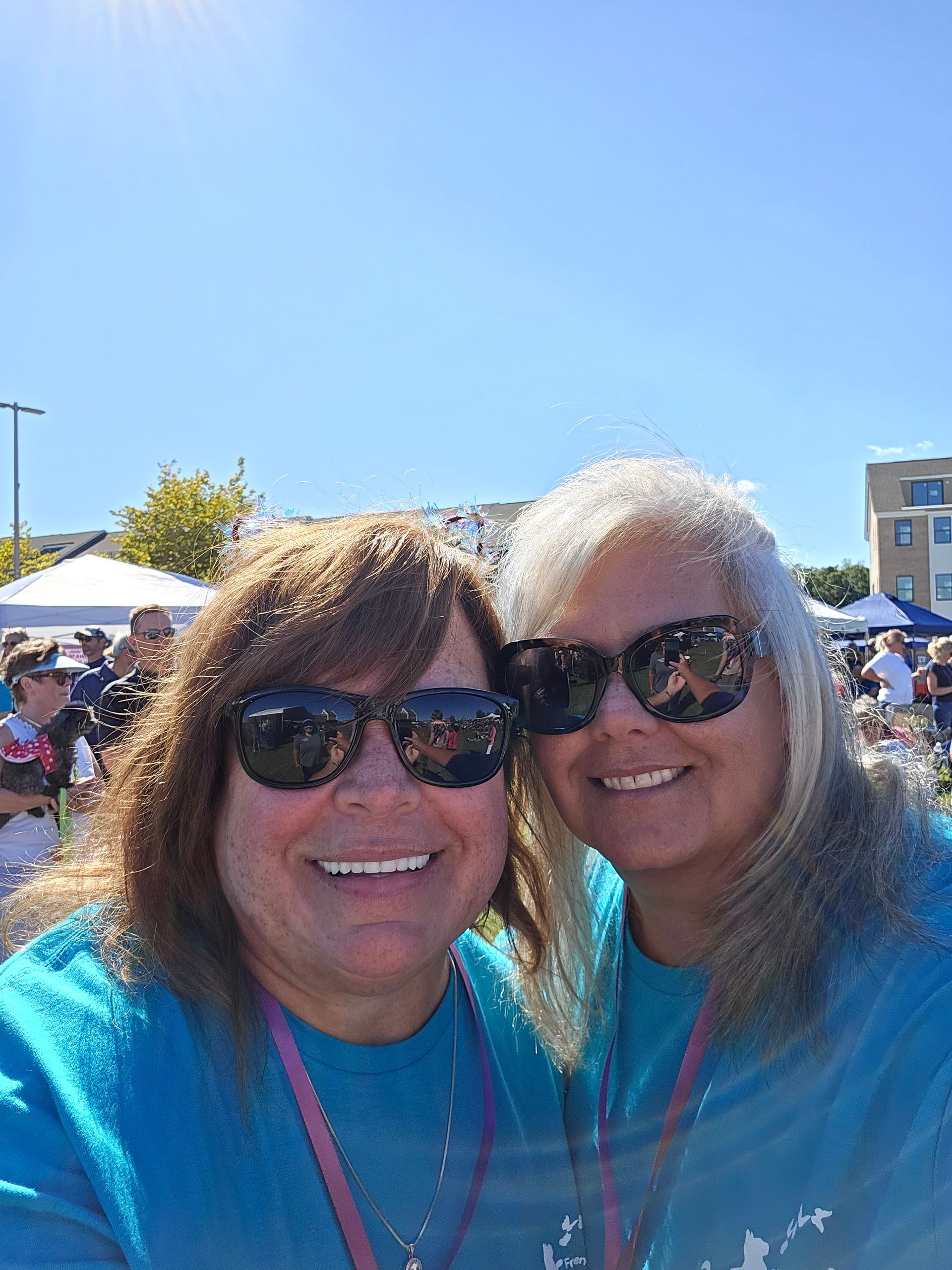 Two women wearing sunglasses and blue shirts are posing for a selfie.