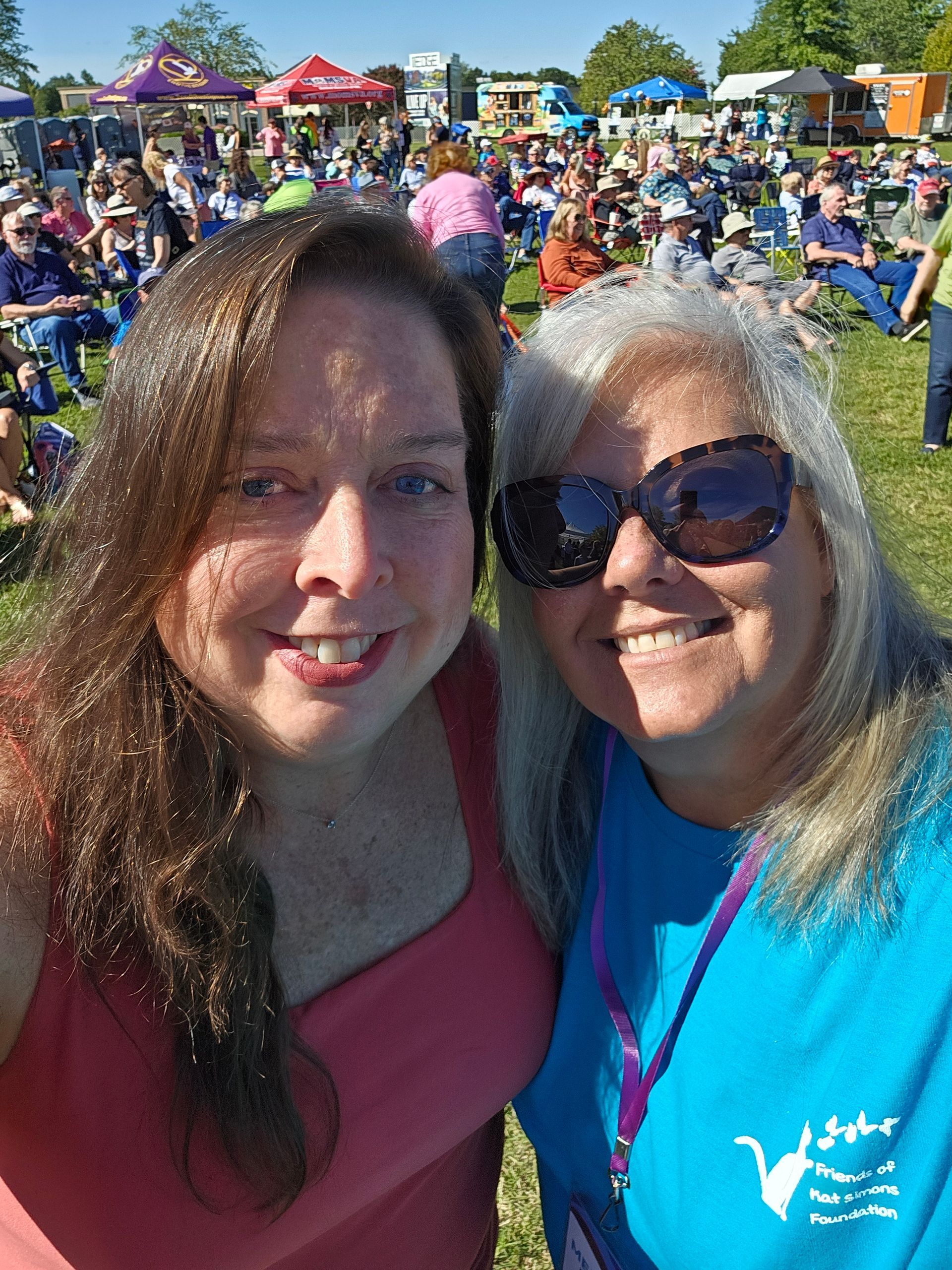 Two women are posing for a selfie in front of a crowd at a festival.