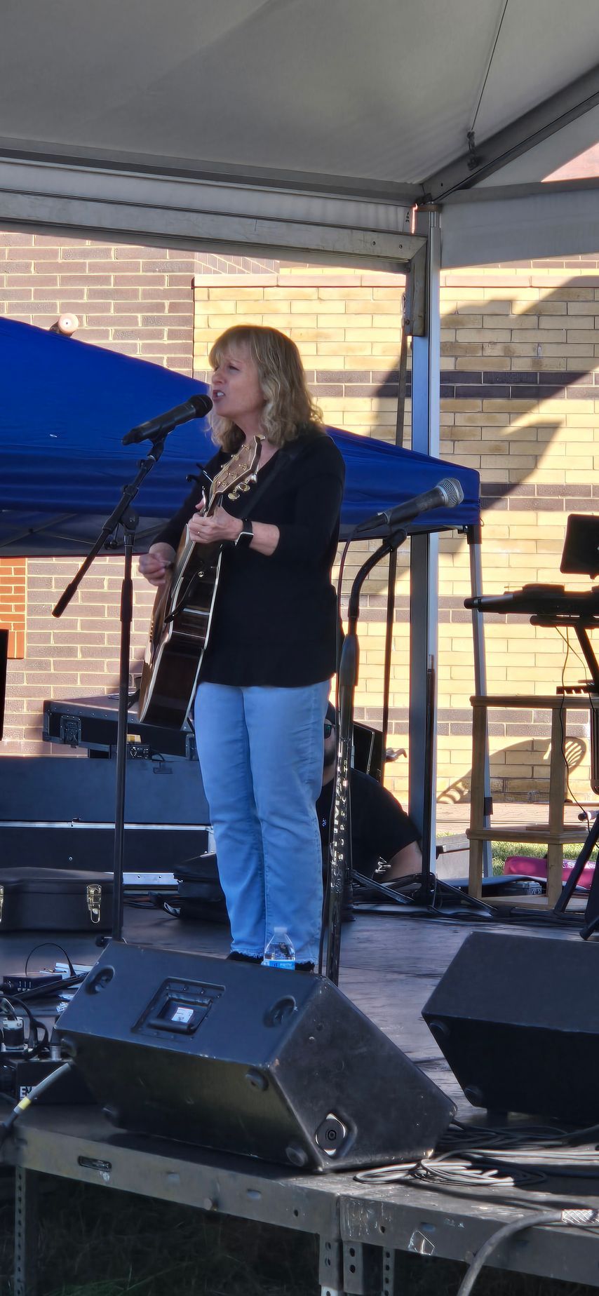 A woman is standing on a stage playing a guitar and singing into a microphone.