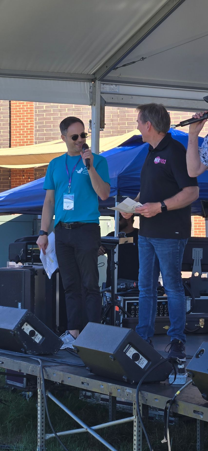 Two men are standing on a stage talking into microphones.