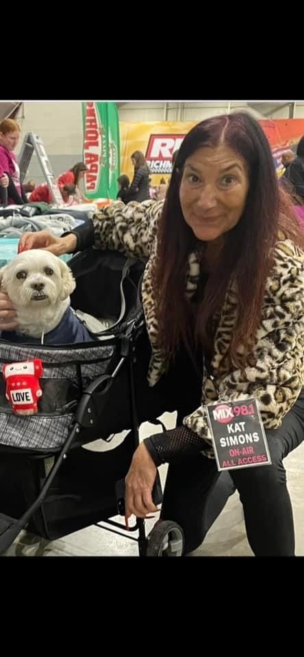 A woman is sitting next to a small white dog in a stroller.