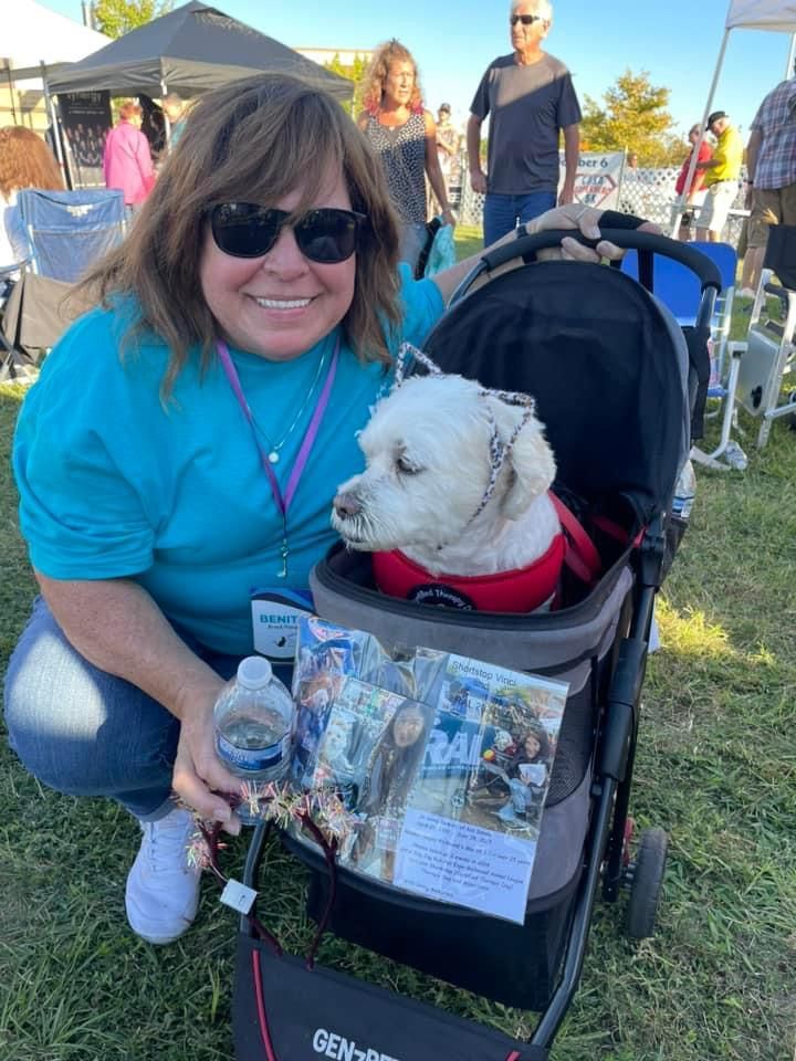 A woman is kneeling down next to a dog in a stroller.