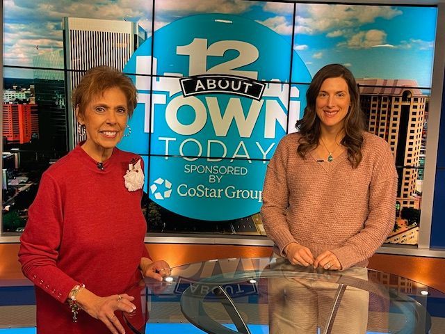 Two women are standing in front of a 12 about town today sign.