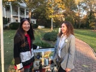 Two women are standing next to each other on a sidewalk in front of a house.