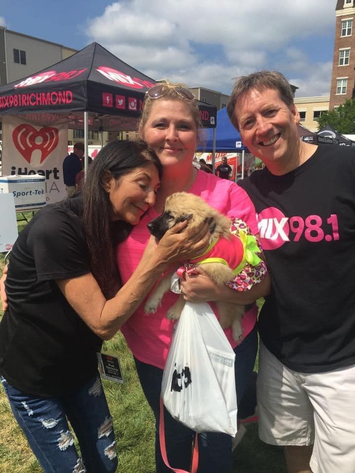 A group of people holding a puppy in front of a tent that says 10x98.1.