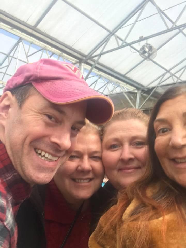 A group of people are posing for a selfie in a greenhouse.