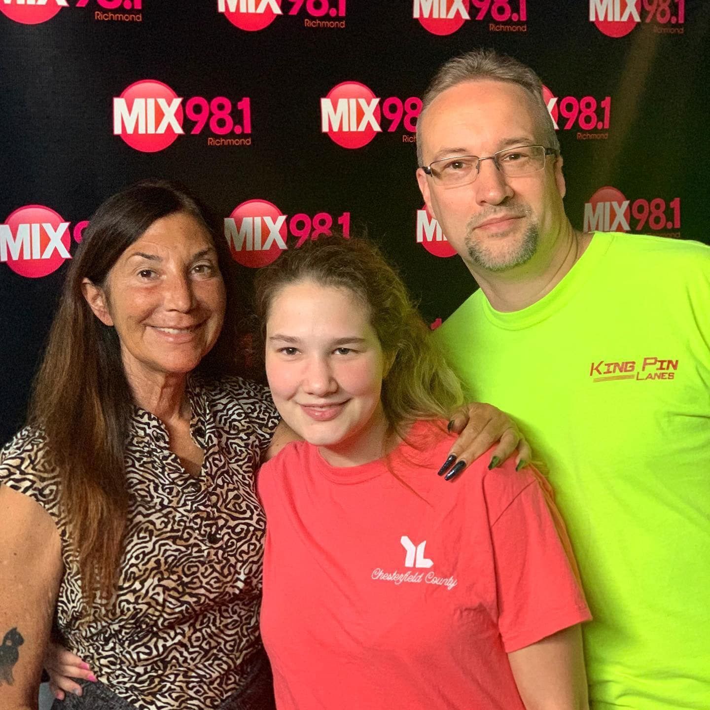 Three people posing for a picture in front of a mix 98.1 banner