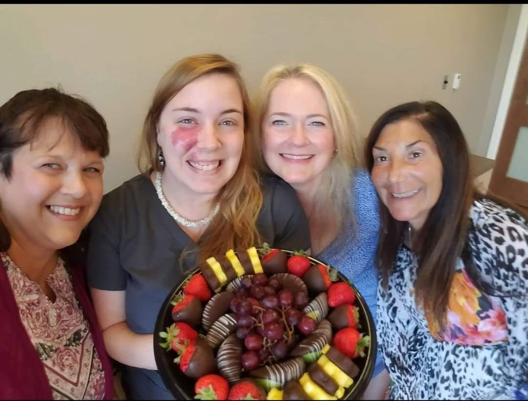 Four women are posing for a picture with a tray of chocolate covered strawberries
