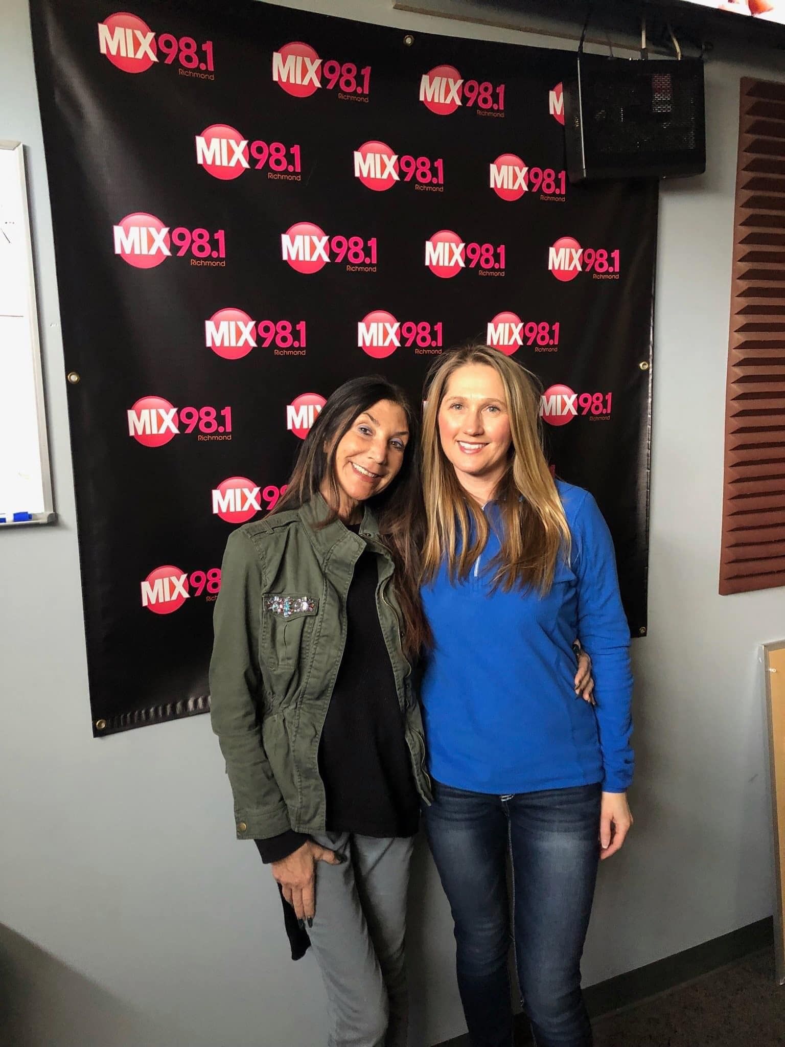 Two women are posing for a picture in front of a mix 98.1 banner