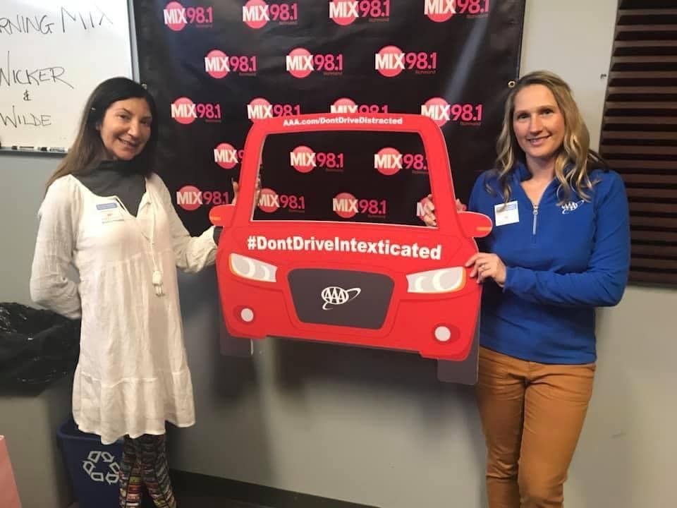 Two women standing next to each other holding a red car with the words 