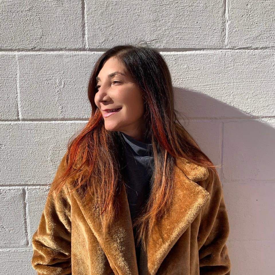 A woman in a fur coat is standing in front of a brick wall.