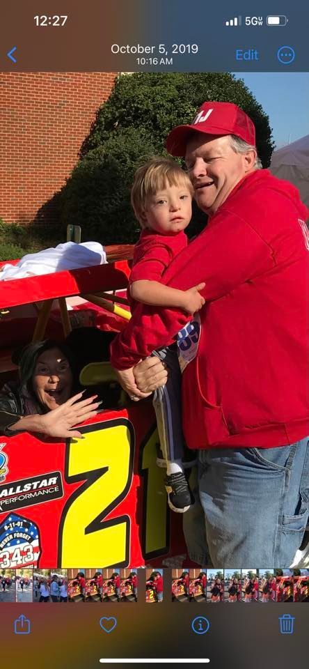 A man is holding a little boy in front of a race car.