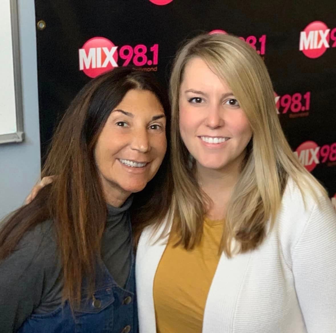 Two women are posing for a picture in front of a sign that says mix 98.1