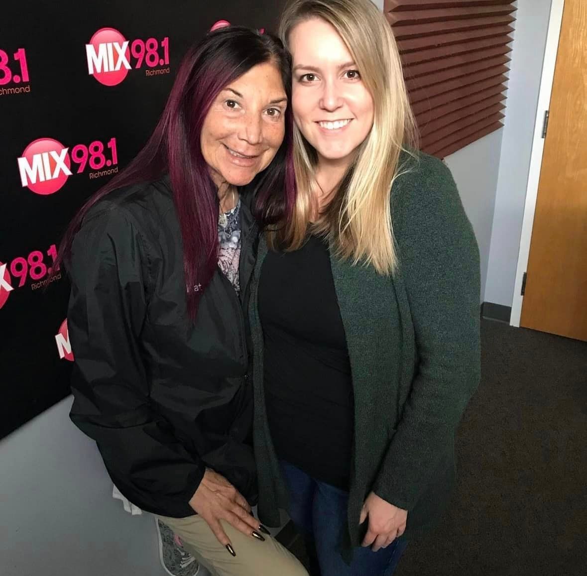 Two women are posing for a picture in front of a sign that says mix 98.1