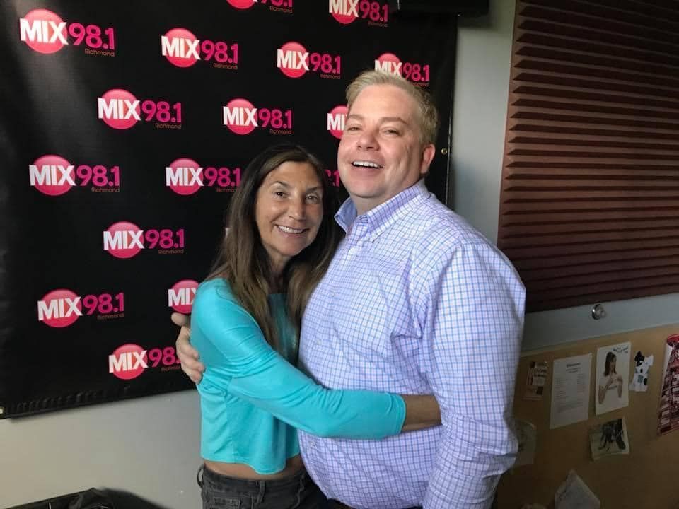 A man and a woman are hugging in front of a mix 98.1 sign.