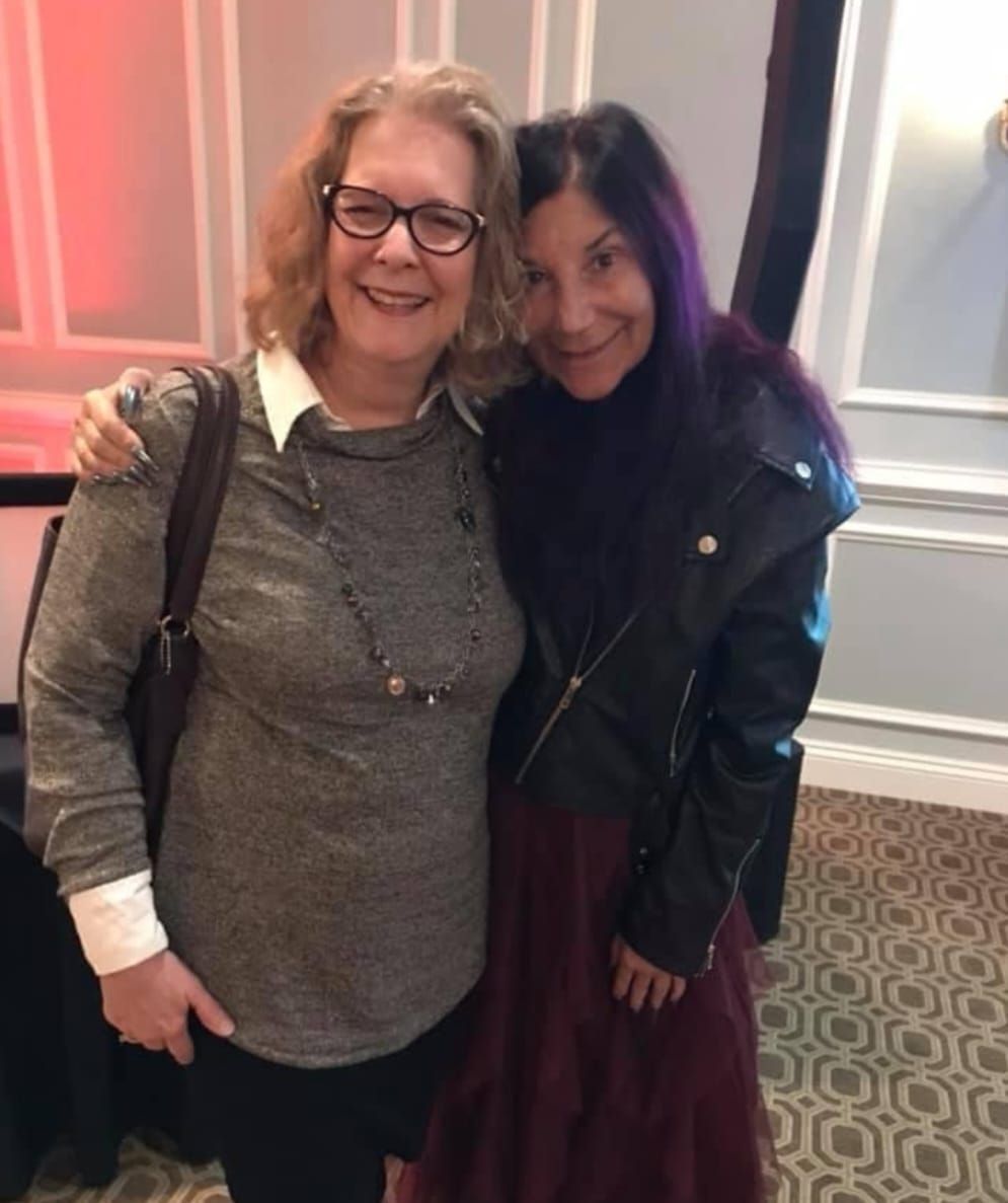 Two women are posing for a picture and one has purple hair