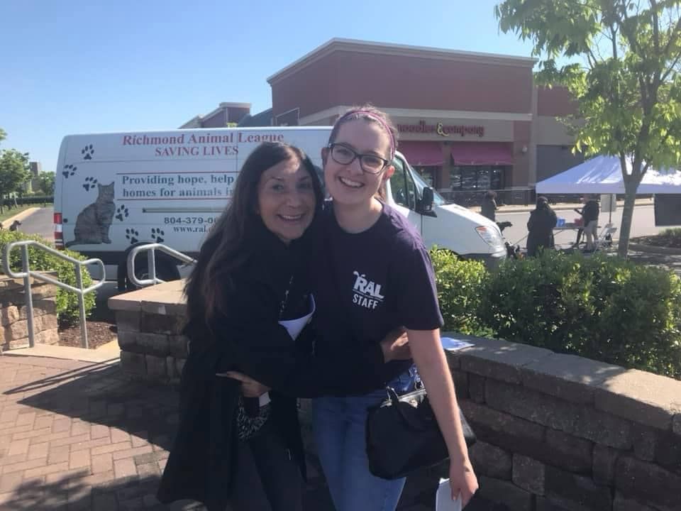 Two women are posing for a picture in front of a white van.