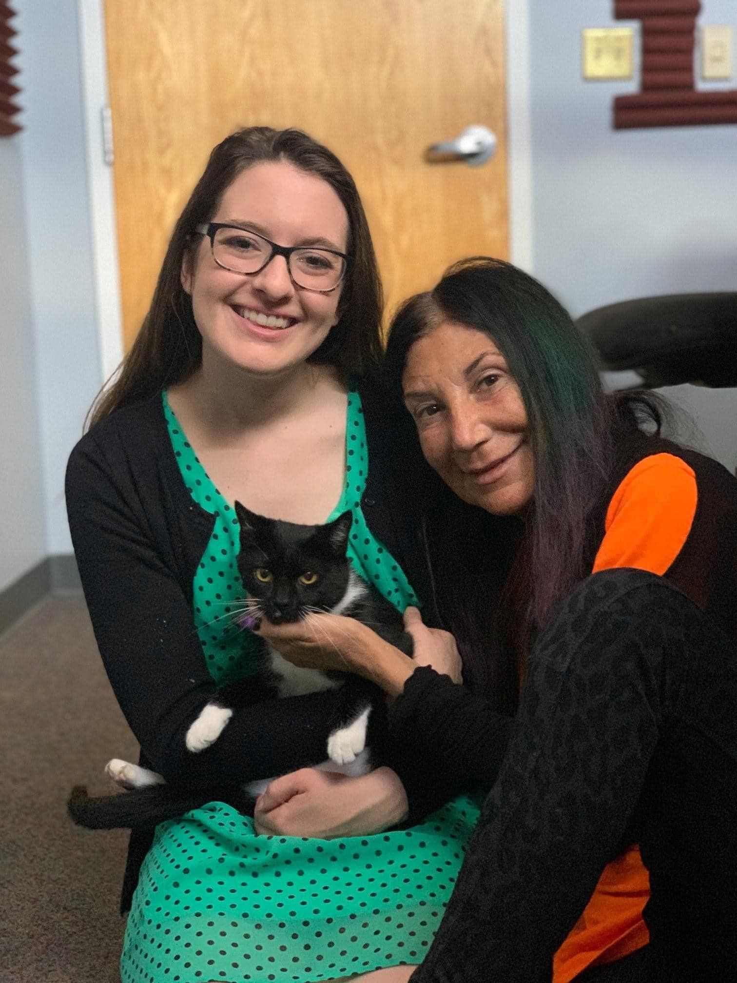 Two women are sitting next to each other holding a black and white cat.