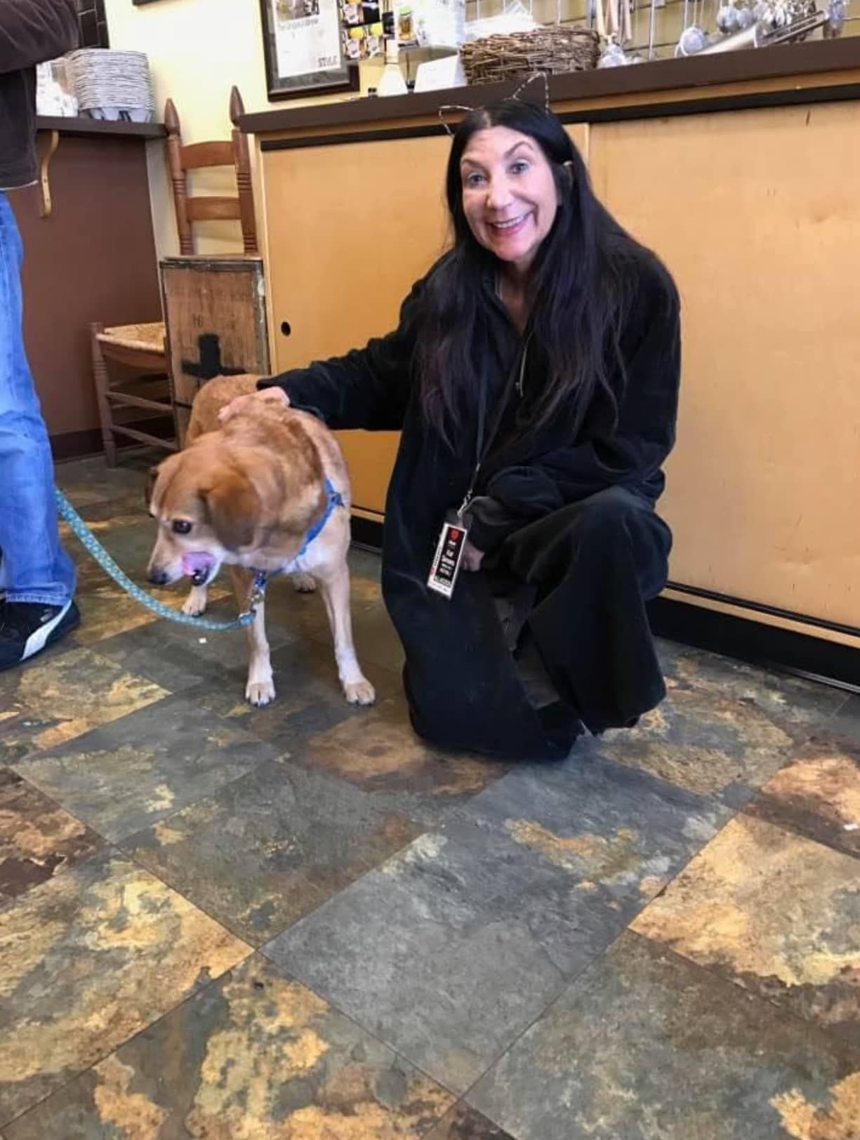 A woman is kneeling down next to a dog on a leash.