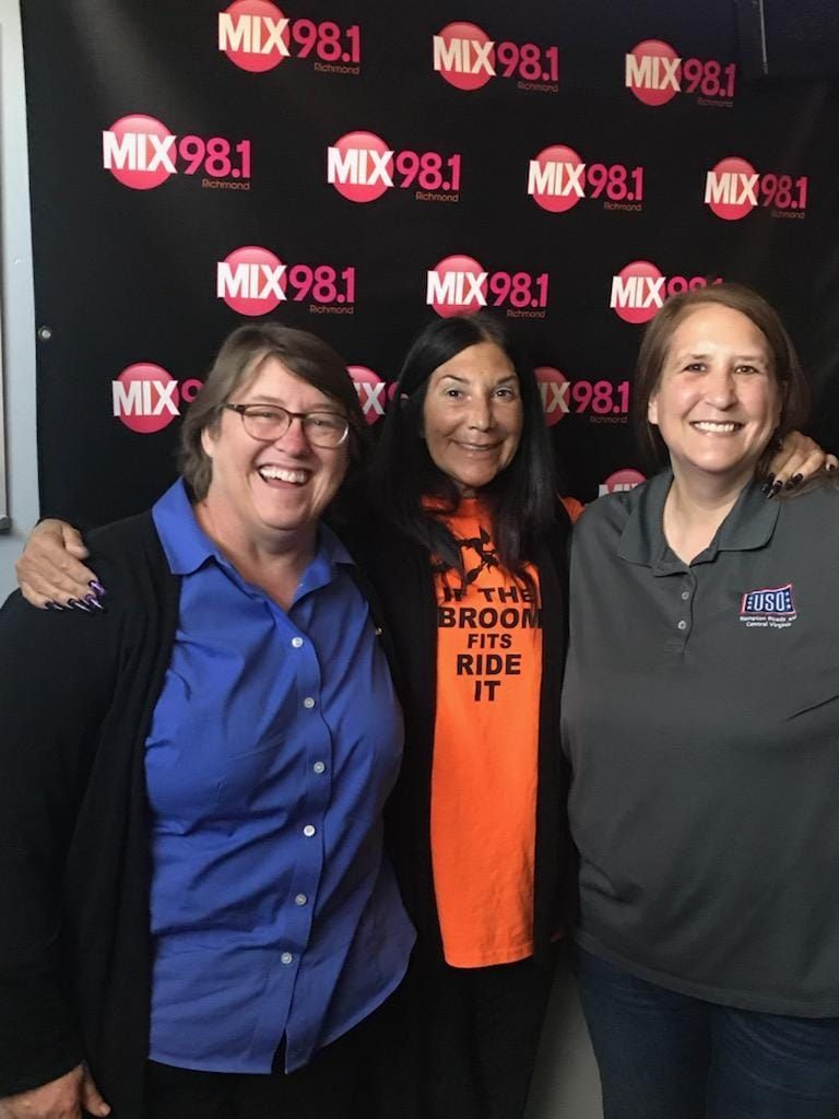 Three women are posing for a picture in front of a wall that says mix 98.1