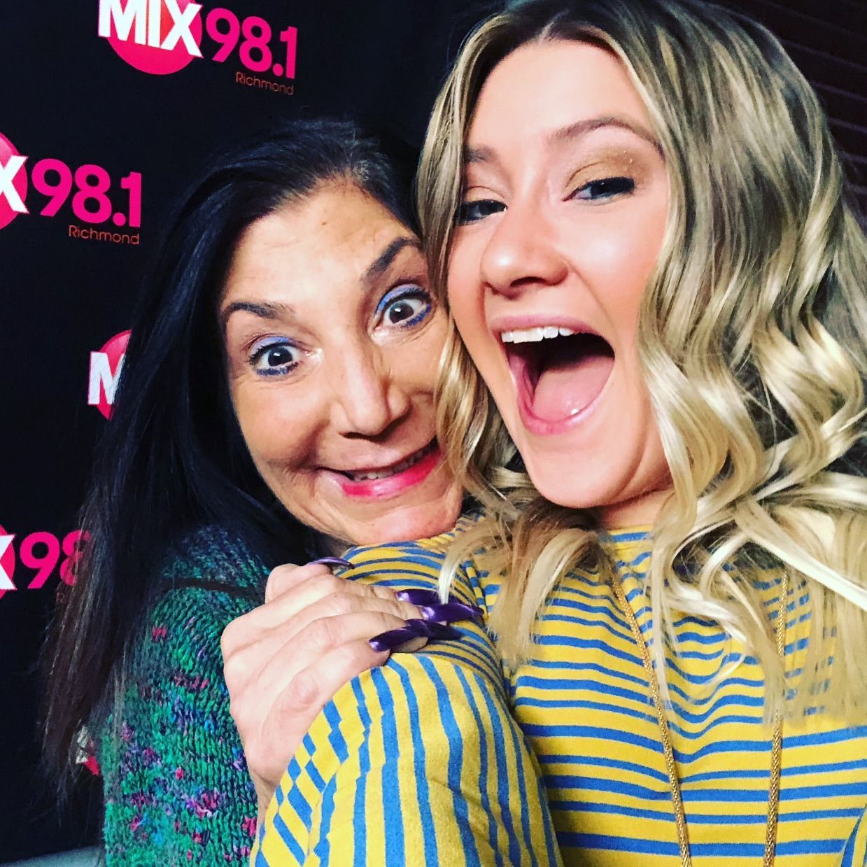Two women are posing for a picture in front of a sign that says mix 98.1