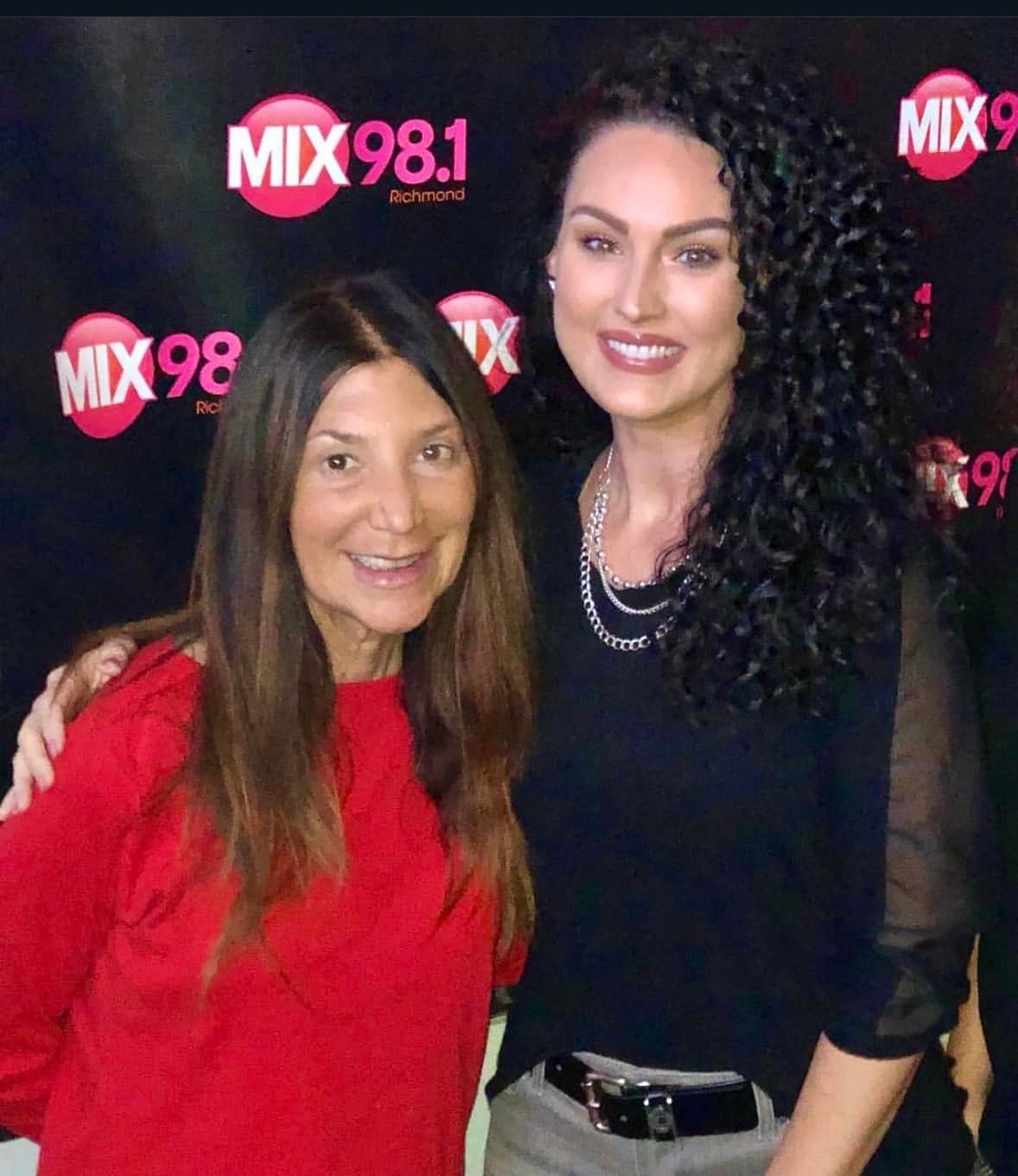 Two women are posing for a picture in front of a sign that says mix 98.1