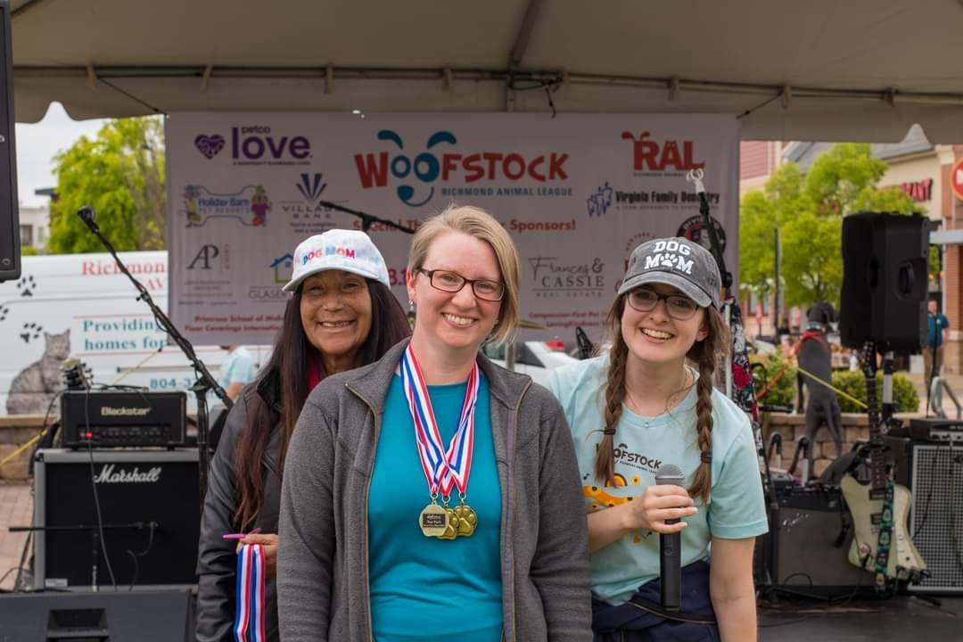 Three women are posing for a picture in front of a sign that says woofstock.