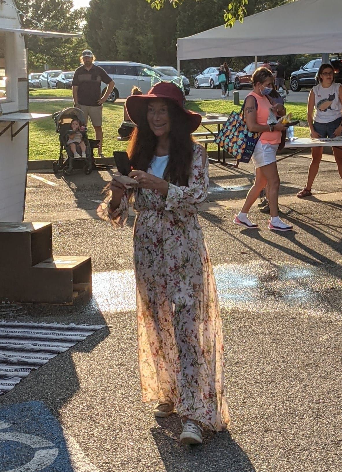 A woman wearing a hat and a long dress is standing in a parking lot.