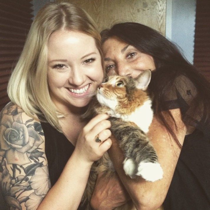 Two women are holding a cat and smiling for the camera
