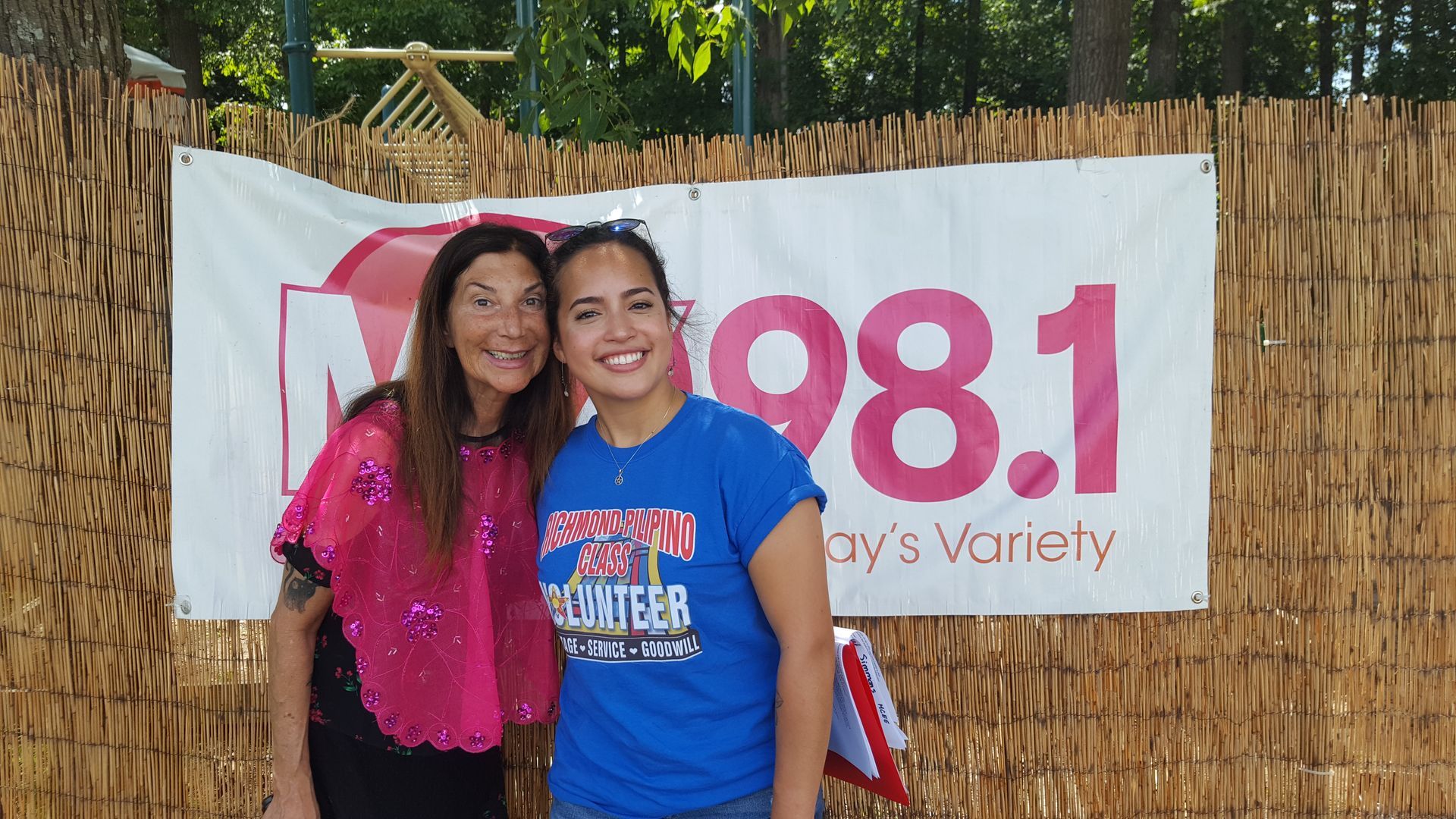 Two women standing in front of a sign that says 98.1