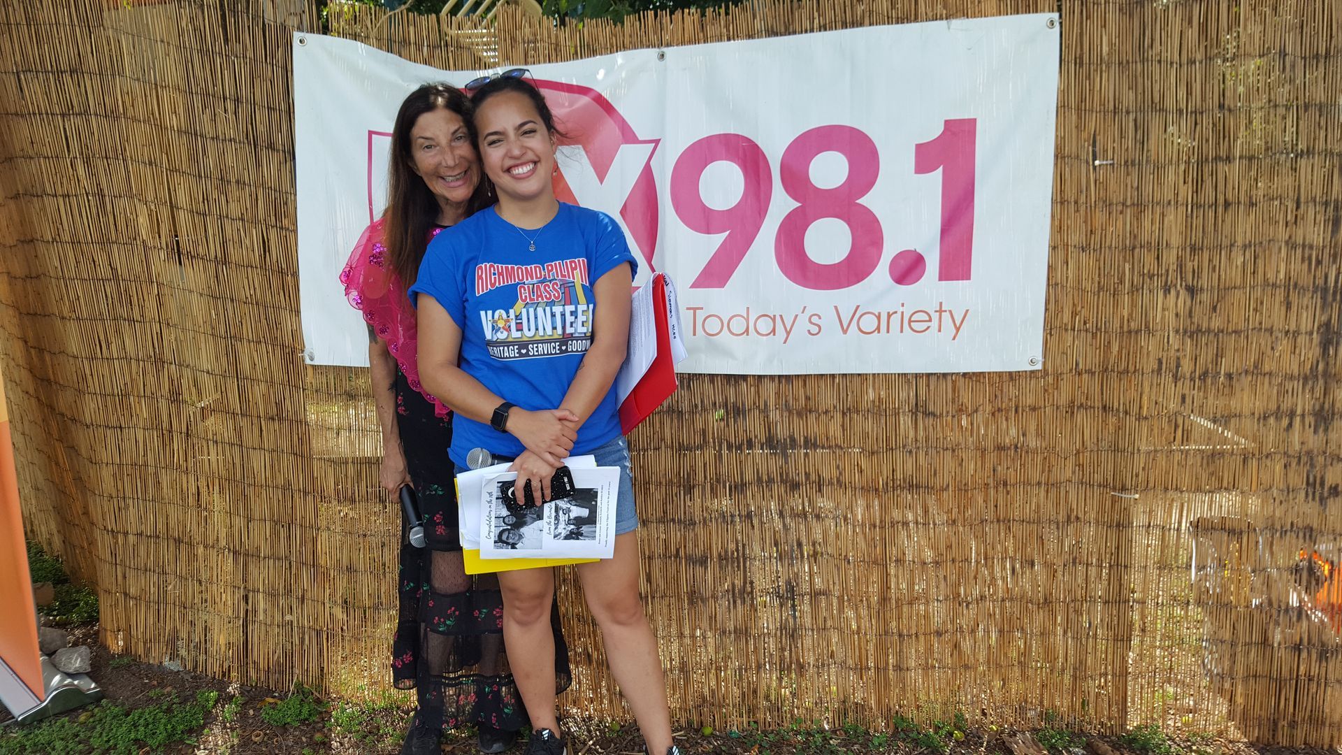 Two women standing in front of a sign that says 98.1