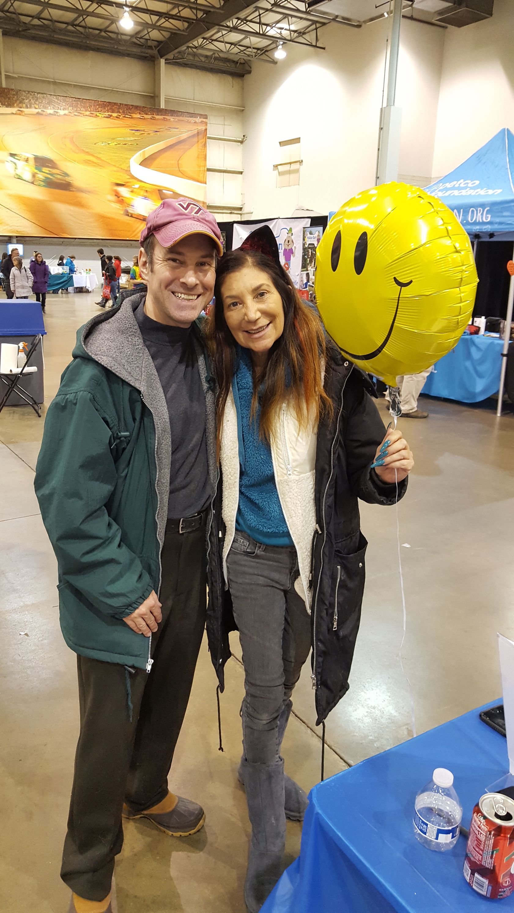 A man and a woman are posing for a picture while holding a smiley face balloon.