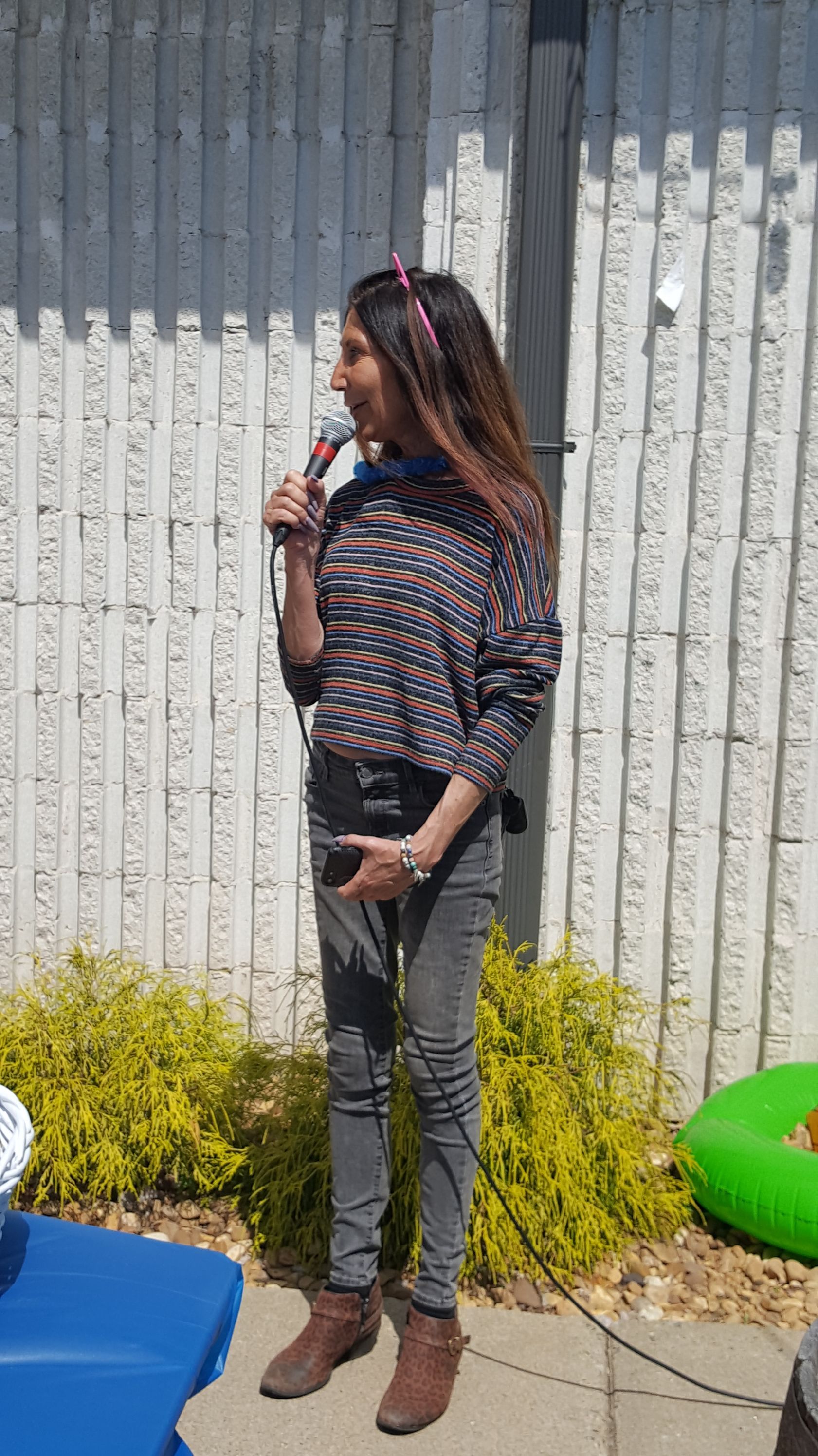 A woman is standing in front of a fence holding a microphone.