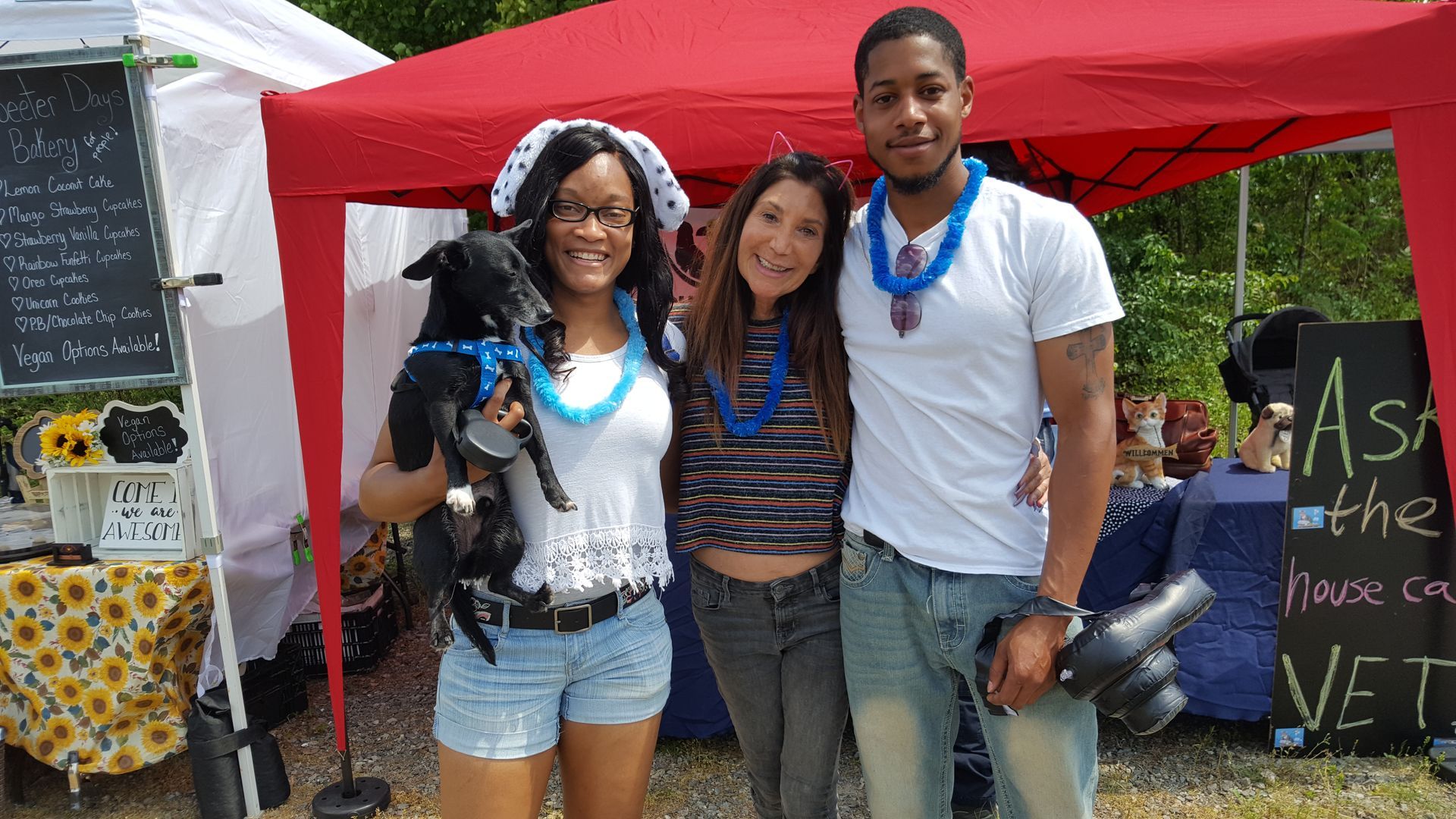 Three people are posing for a picture with a dog in front of a tent.