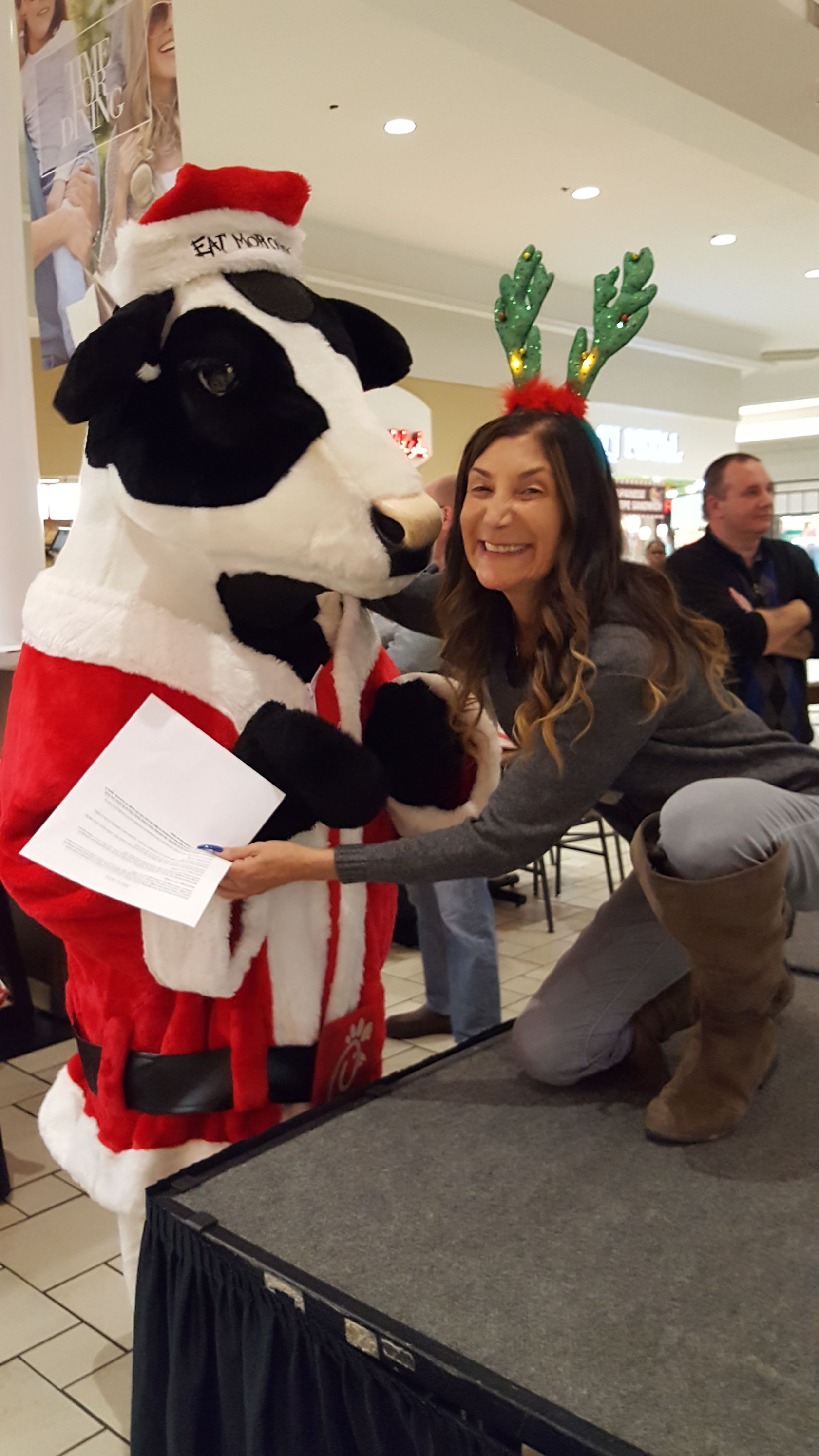 A woman is kneeling next to a stuffed cow dressed as santa claus