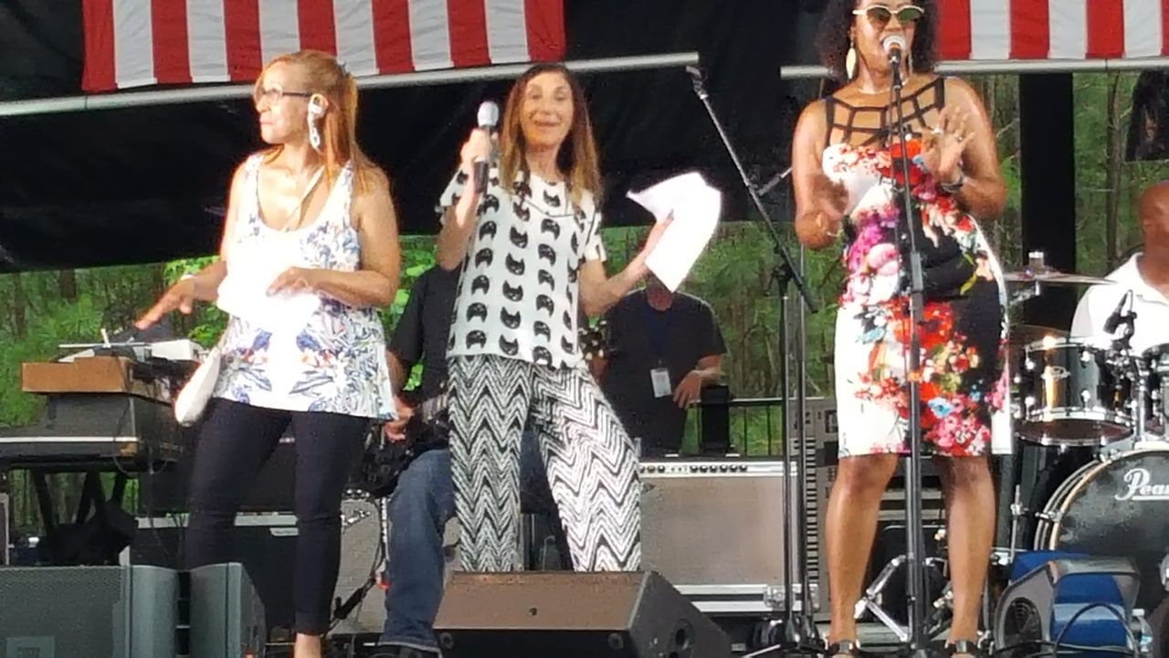 A group of women are standing on a stage singing into microphones.