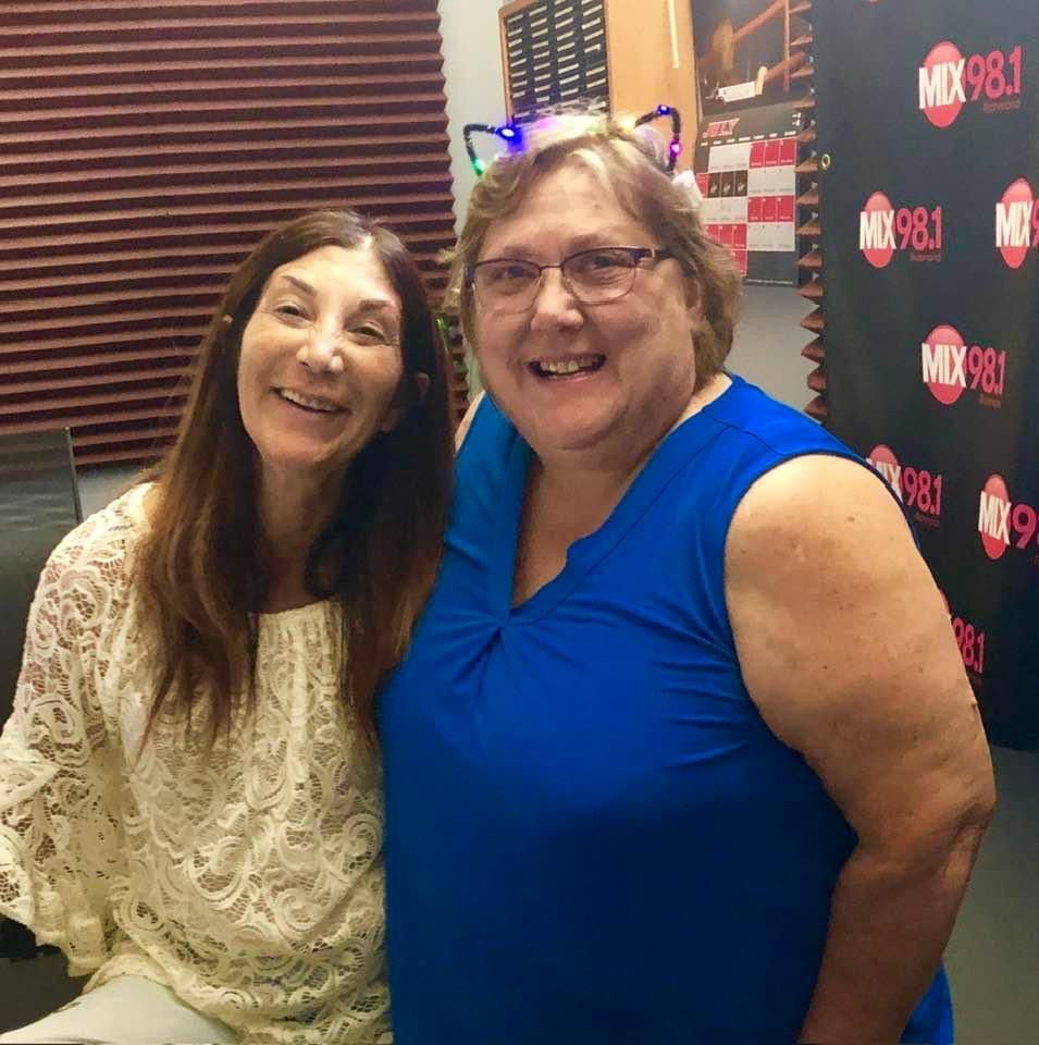 Two women are posing for a picture in front of a wall that says mix 98.1
