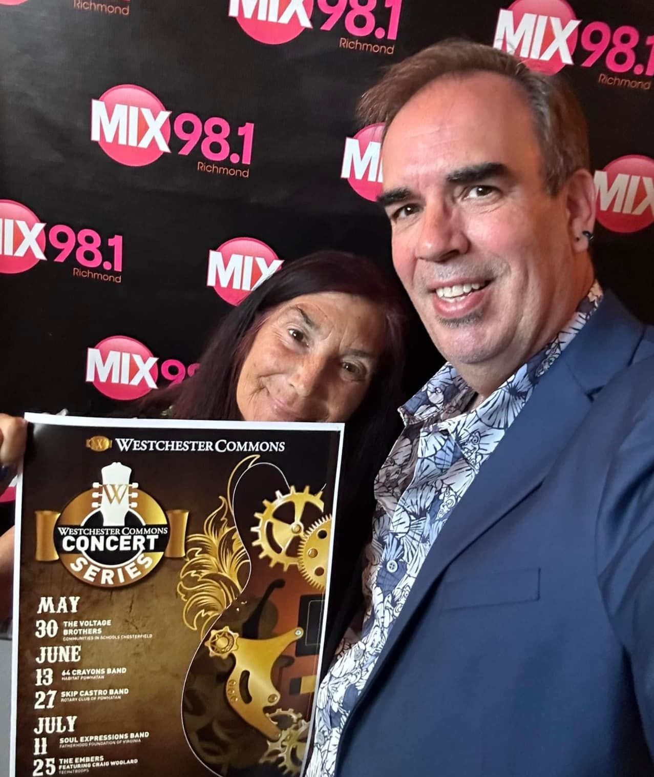 A man and woman are posing for a picture in front of a mix 98.1 banner