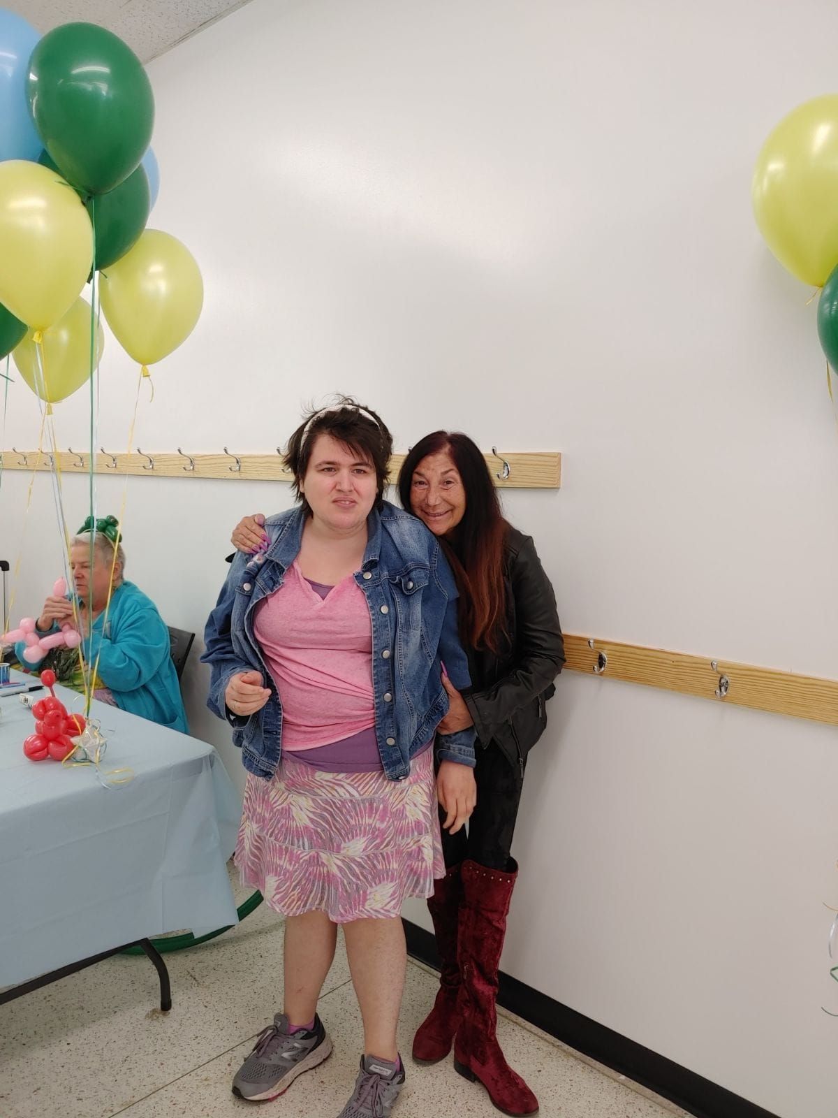 Two women are standing next to each other in a room with balloons.