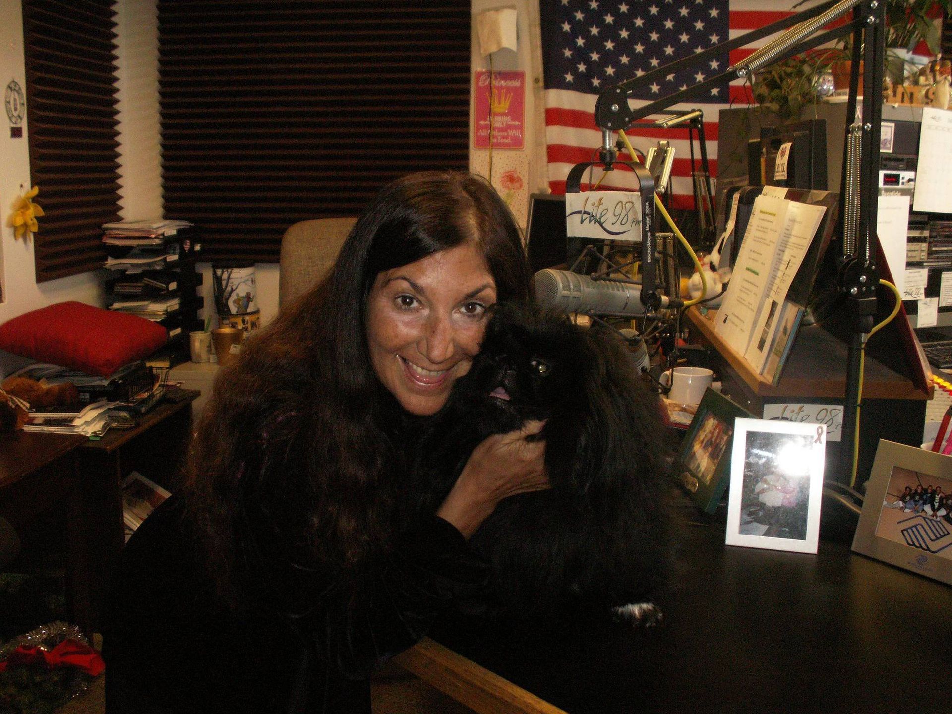 A woman holding a black dog in front of an american flag