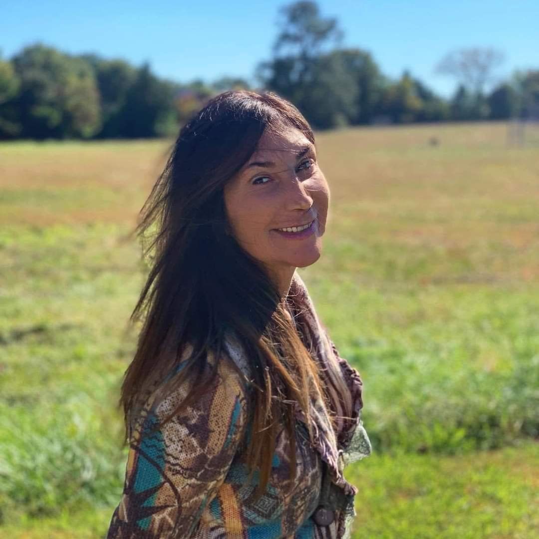 A woman is standing in a field of grass and smiling at the camera.