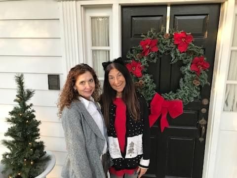Two women are standing in front of a door with a christmas wreath on it.
